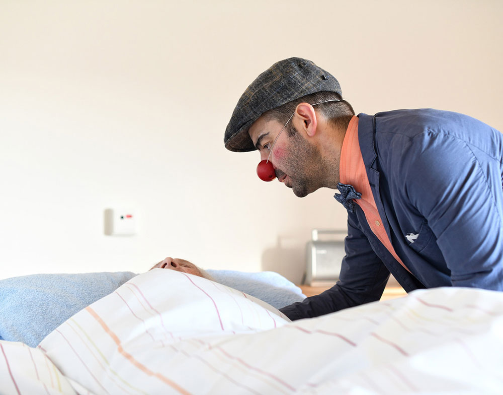 Ein Clown beugt sich liebevoll über ein Krankenbett